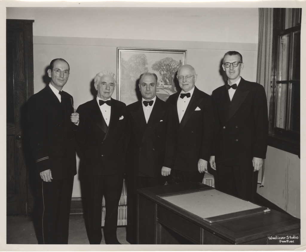 A photograph of five men wearing tuxedos, facing the camera.