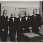A photograph of five men wearing tuxedos, facing the camera.